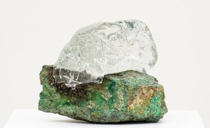 A sculpture consisting of a translucent crystal atop a green stone.
