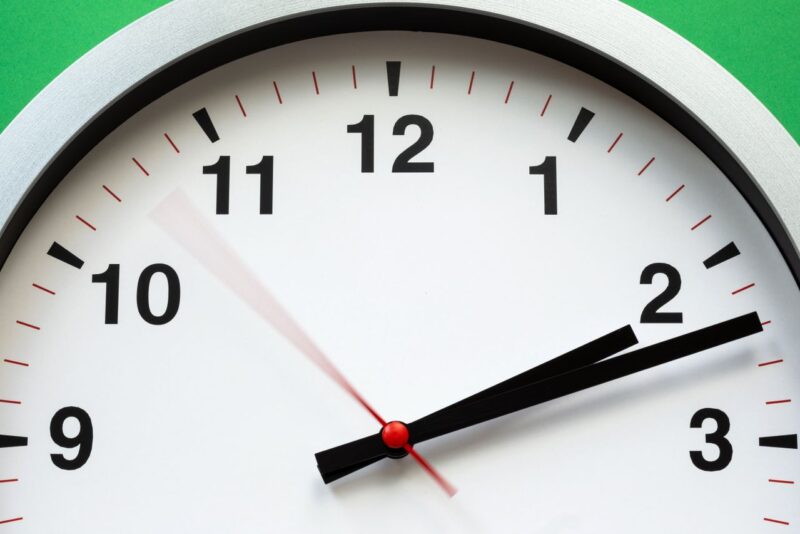 Closeup on top half of clock with a moving red second hand.