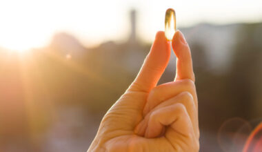 A hand holding a vitamin D softgel up to the sunlight