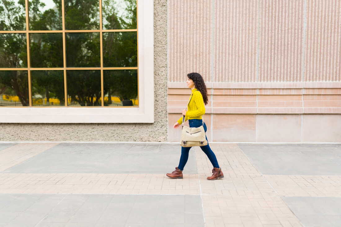 Side profile of a young woman walking carrying a messenger bag.