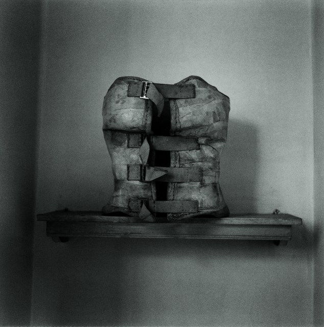 A vintage medical torso brace with buckled straps sitting on a wooden shelf.
