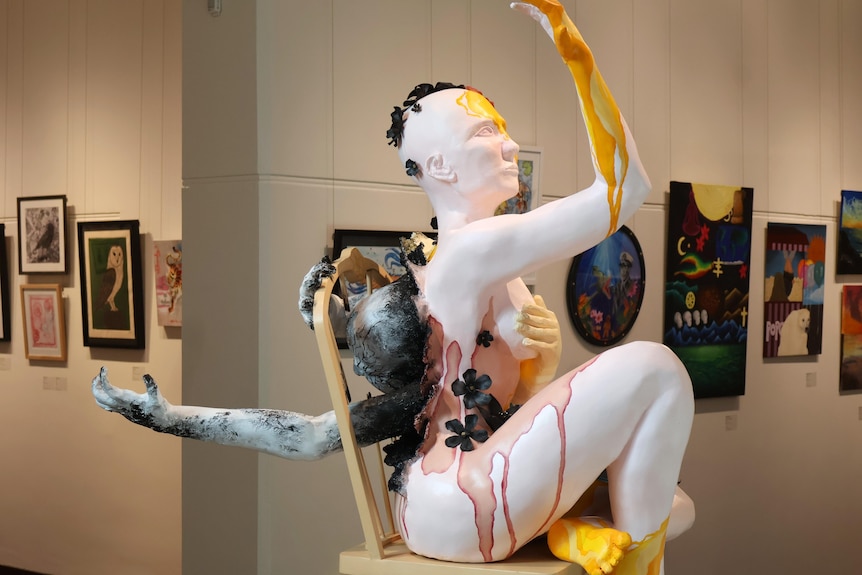 A sculpture of a person sitting in a chair with splashes of paint.