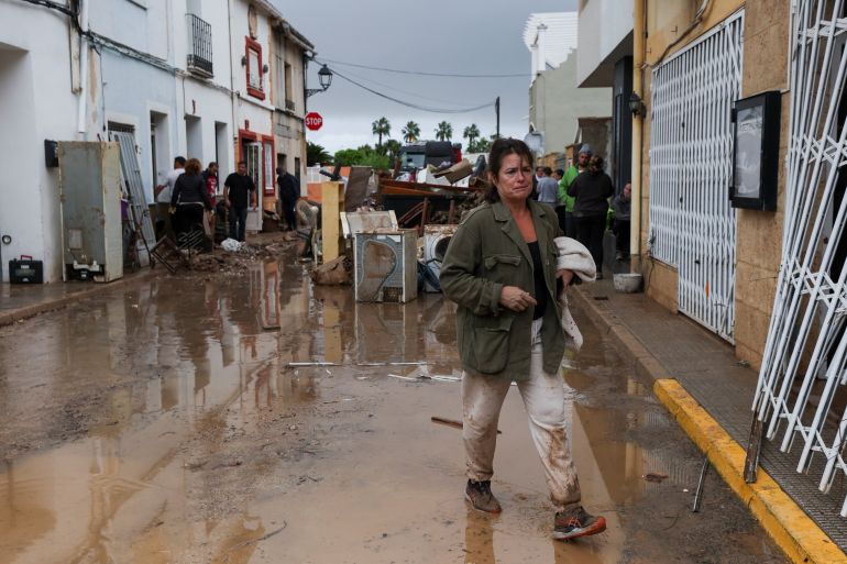 A woman walks on a mud-covered street, following torrential rains, which caused floods in eastern Spain, in Els Poblets, Alicante province, Spain, October 19, 2026 [Eva Manez/Reuters]