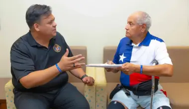 Two people sit in a clinic waiting area, talking while reviewing a clipboard during a discussion about stress.