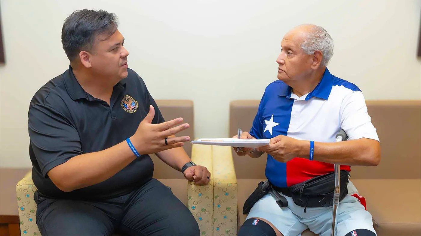 Two people sit in a clinic waiting area, talking while reviewing a clipboard during a discussion about stress.