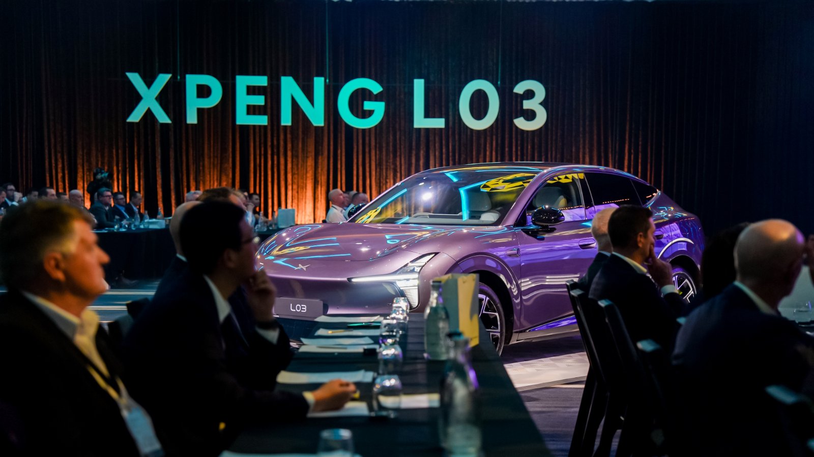 A purple Xpeng L03 SUV displayed among seated guests beneath illuminated XPENG L03 lettering.