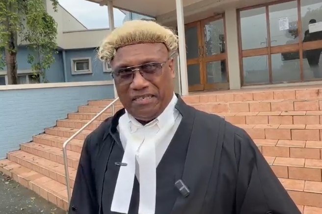 Gabriel Suri, wearing the robes and wig of a lawyer, looks at the camera.