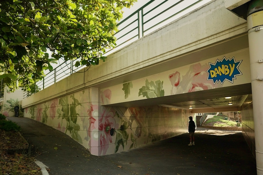 A tree next to a underpass painted in cream, green and pink with the artists signature as 'Danby'.