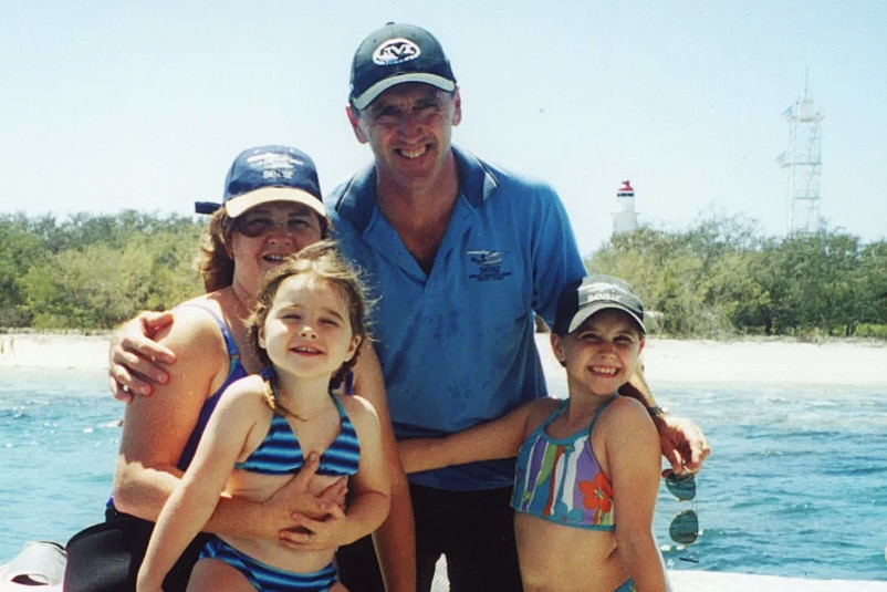 Peter and Julie Gash on a boat with their young daughters, Amy and Chloe, with an island behind them.