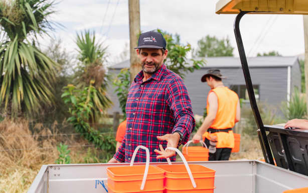 Mike Casey places two large orange buckets in the tray of a farm vehicle