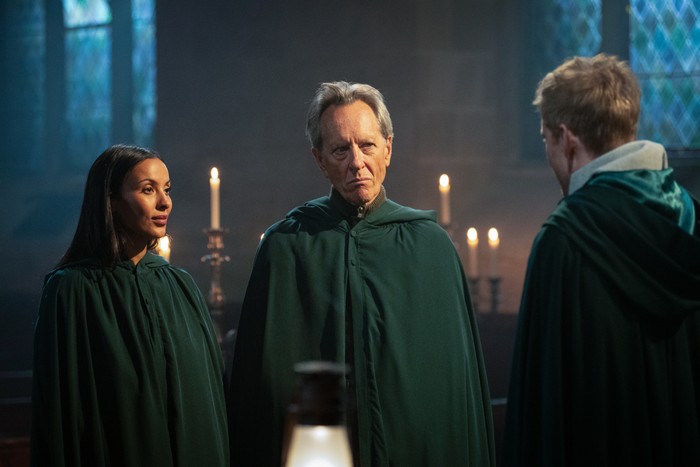 579622,TITLE:The Celebrity Traitors S2 Maya Jama and Richard E Grant in traitors cloaks looking over at James Acaster.