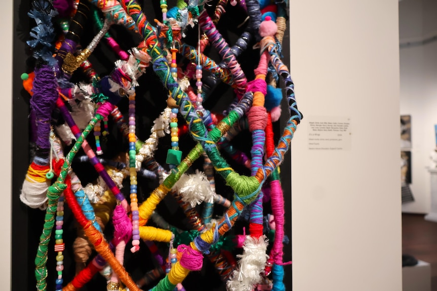 A sculpture of sticks wrapped in colourful yarn on a black backing.