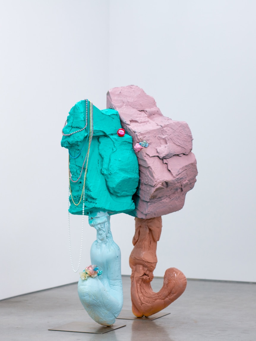 A sculpture made from clay, stell and foam, and painted in bright colours, like two rocks stuck together, with legs.