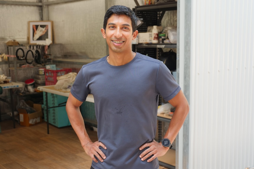 A Malaysian man, Mithram Selvaratnam, stands outside a work shed with hands on his hips and smiles at the camera.