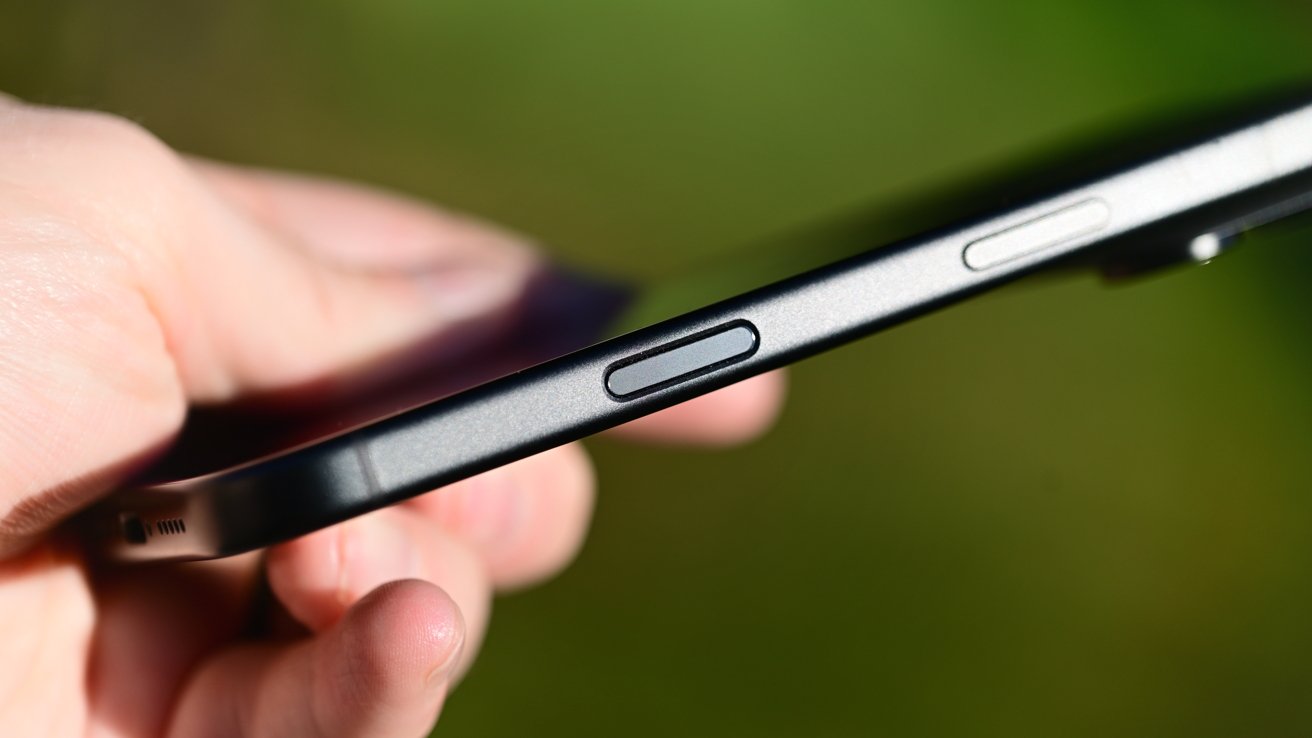 Close-up of a hand holding a slim smartphone sideways, focusing on the side buttons against a softly blurred green background