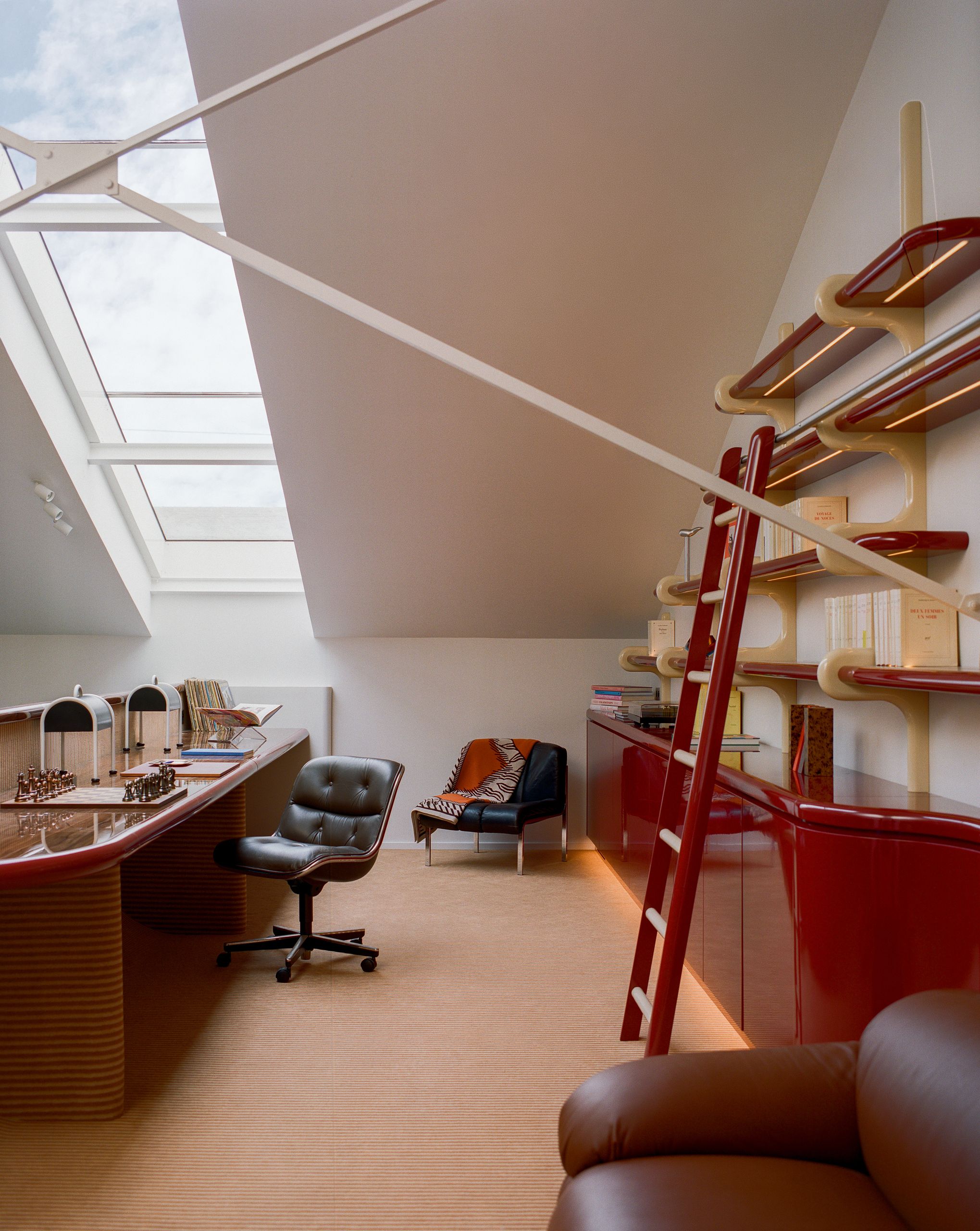 Image of a home office in a mezzanine. There is red lacquer shelving and a matching desk. The decor is mid-century and Space Age-inspired.