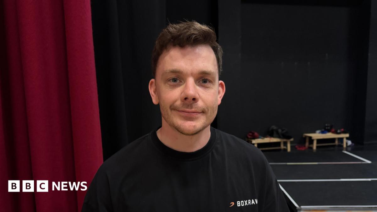 A man looking straight at the camera smilling - he is wearing a black t-shirt.