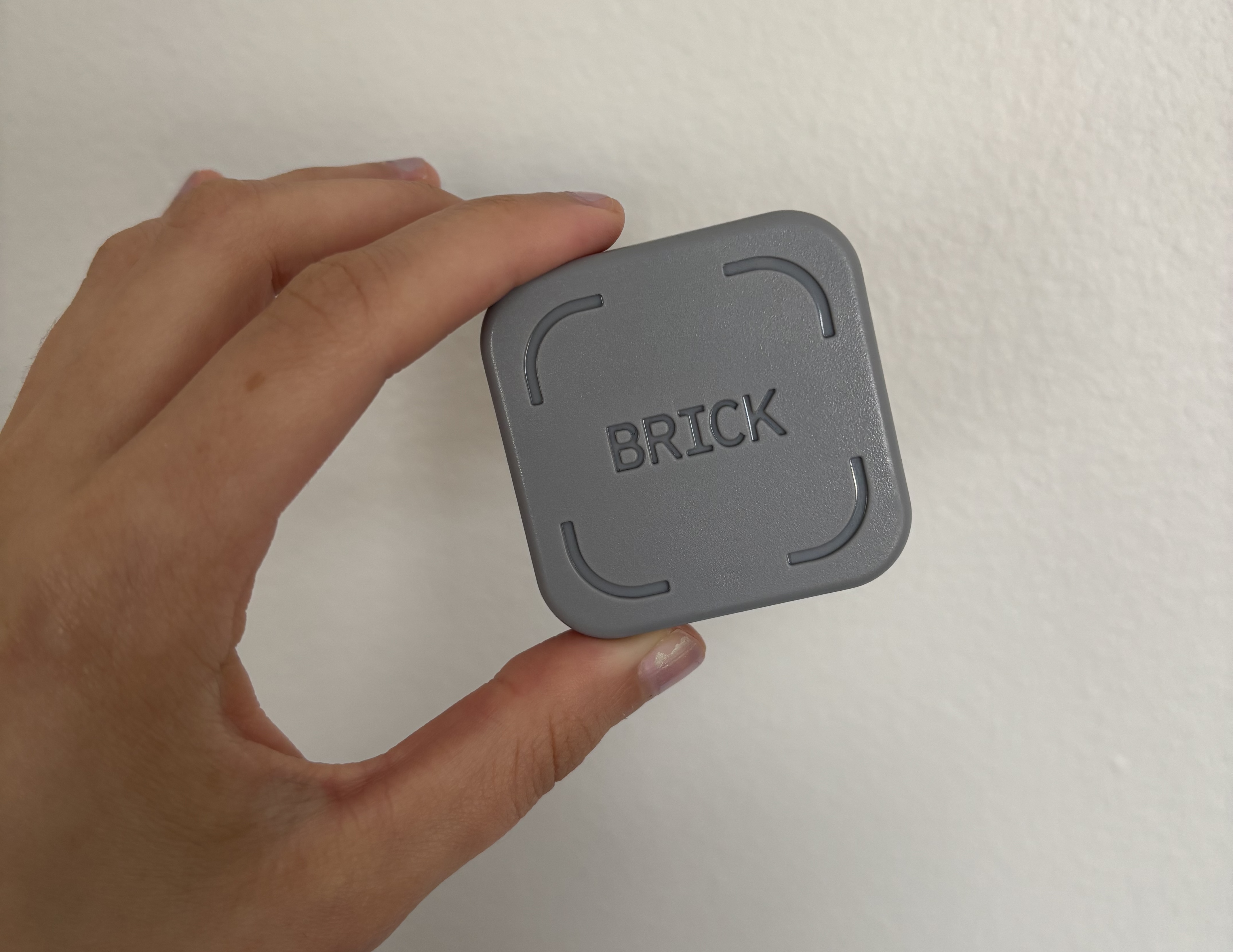 A hand holding the Brick in front of a white wall.