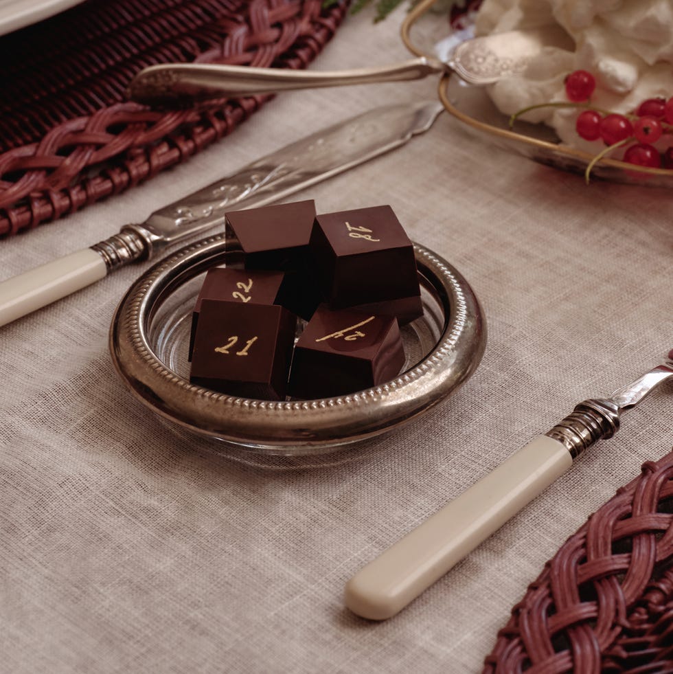 Elegant dining table set with white plates, chocolate squares, whipped cream, berries, and champagne flutes on woven placemats.