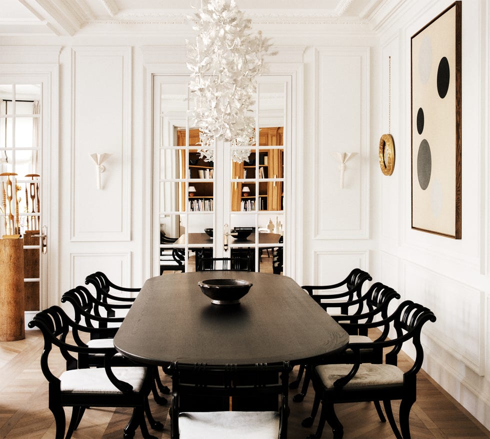 Elegant dining room featuring a large black table, ornate chairs, and a striking chandelier in a bright, minimalist space.