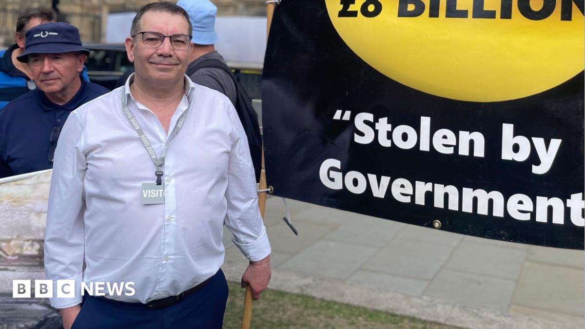 Picture of a middle aged white man, in a white shirt standing next to a black and gold banner stating: "Saved by Miners. I.O.U £8 billion. Stolen by Government".