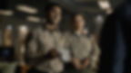 Two sheriff deputies in beige uniforms stand in a dim office; one holds an evidence bag, both looking serious.