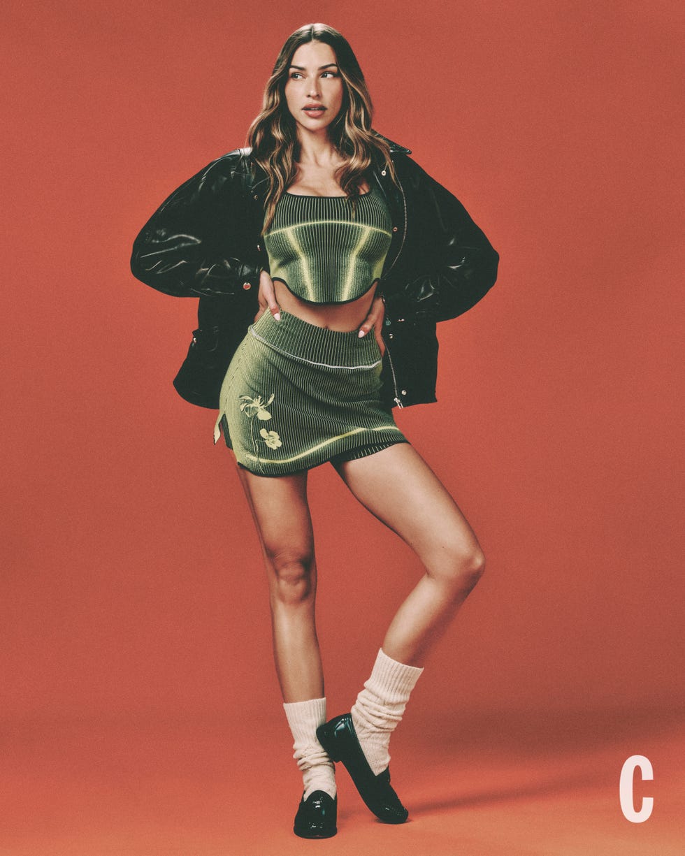 person modeling in green outfit with black jacket against an orange background. person modeling in green outfit with black jacket against an orange background.