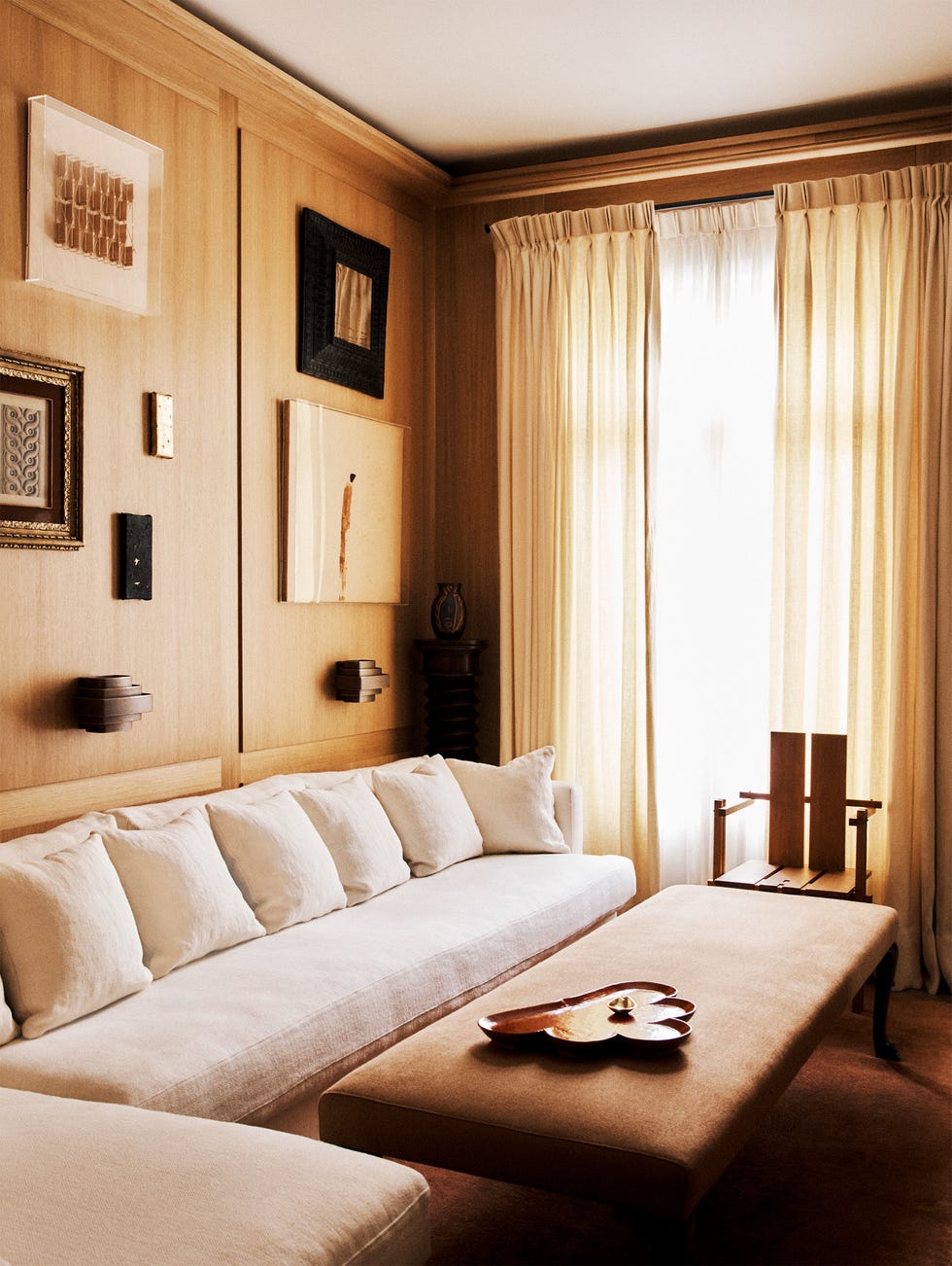 Cozy living room featuring a white sofa, wooden accents, decorative art on walls, and natural light from curtains.