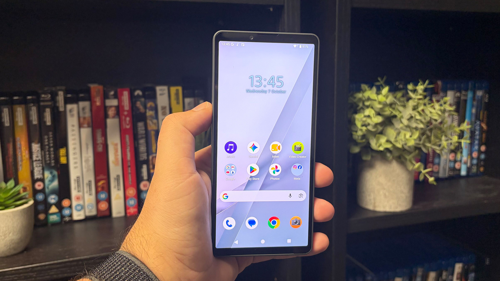 Sony Xperia 10 VIII smartphone held in hand in front of bookcase, on screen are apps