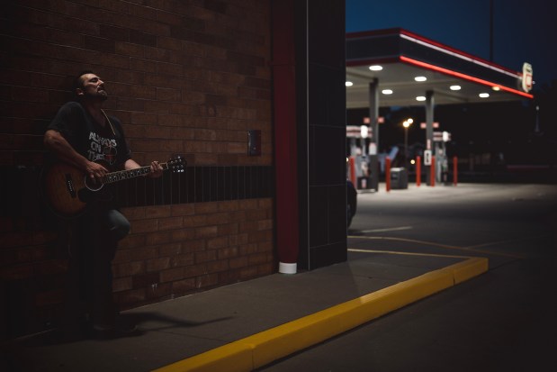 Benton resident Charlie Mopps sings and plays his guitar while his girlfriend finishes working her shift at a gas station on June 3, 2026. (E. Jason Wambsgans/Chicago Tribune)