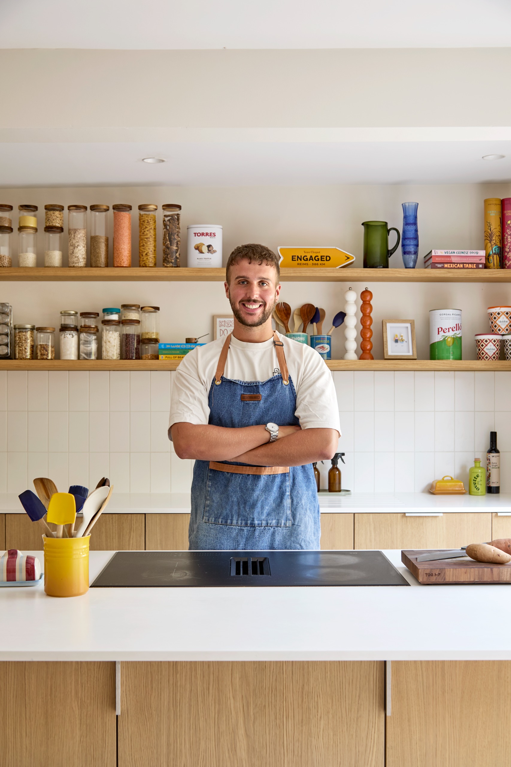 Alfie Steiner standing in his renovated kitchen, with open shelves behind, white tiles, and a white countertop