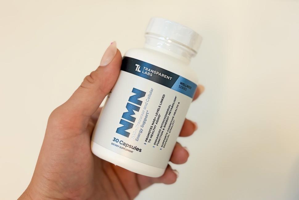 Closeup of a woman's hand holding a bottle of Transparent Labs NMN