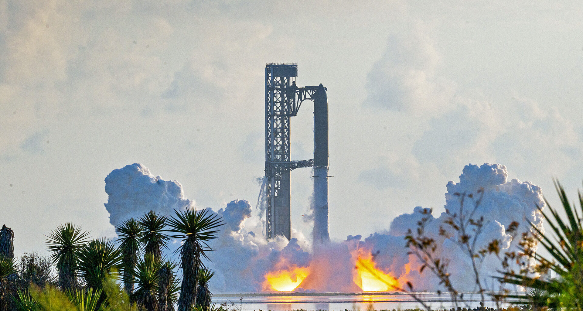 A large rocket stands on a launchpad as flames and thick clouds of smoke rise from its base.