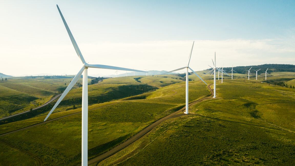 Wind turbines tower above the earth in a rural setting, drawing renewable energy as they spin. Sustainable energy and green technology that considers the environment. Shot in Washington state, USA.