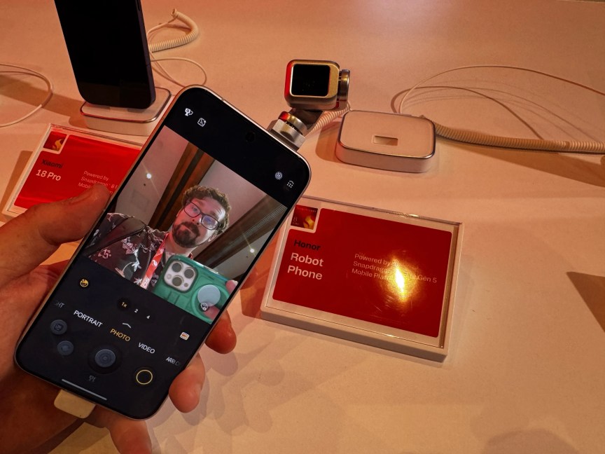 A phone with a camera on a gimbal arm poking out of the back points forward over the phone and the screen shows what it's pointing at -- a man.