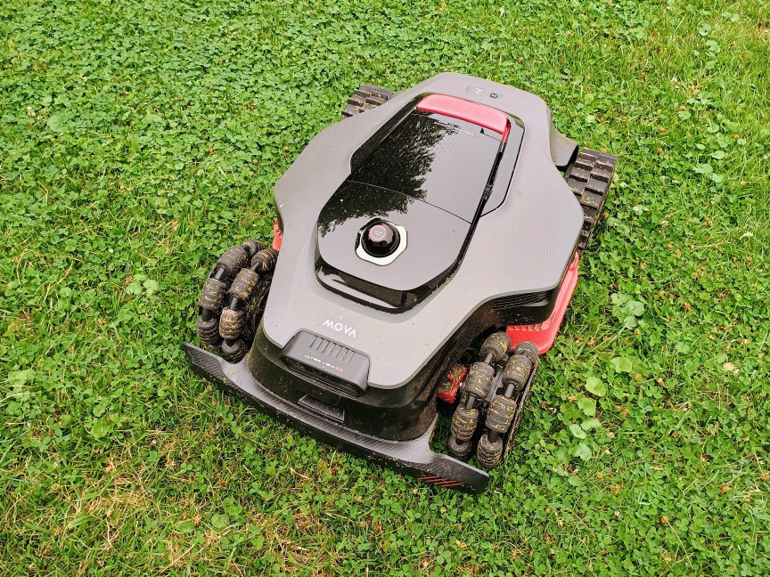 A black robot mower by Mova with red accents sits in a bright green lawn.