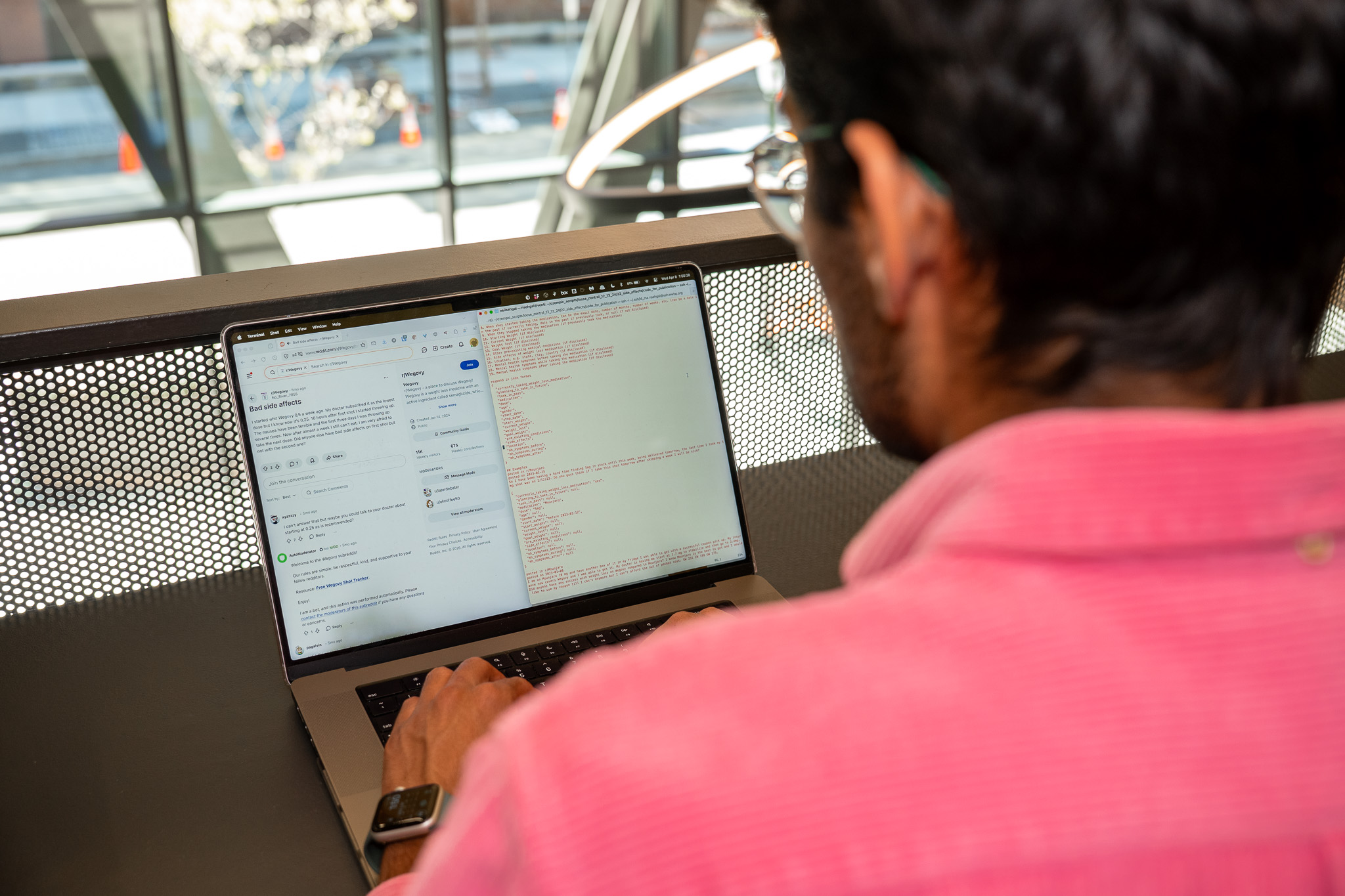Looking over the shoulder of a man in a pink shirt, who is typing on a laptop with two windows open.