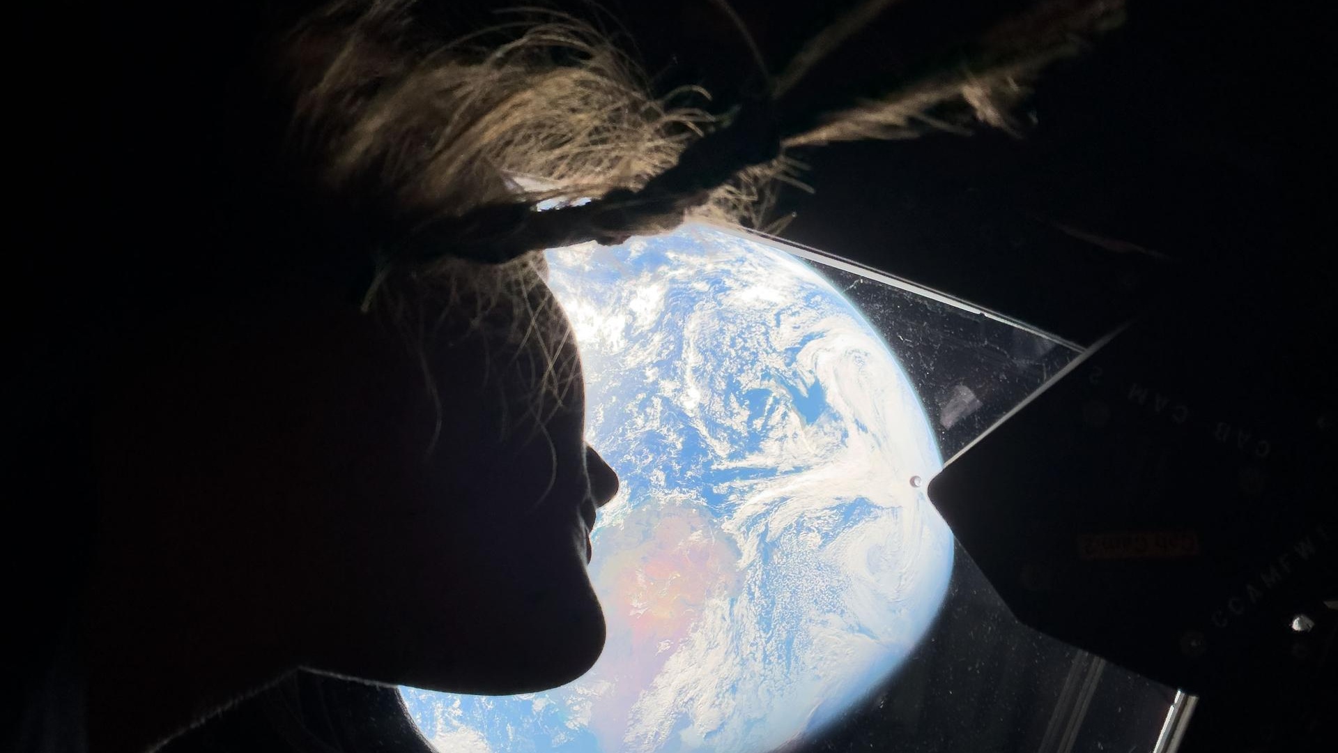The silhouette of a woman looking out the window at Earth.