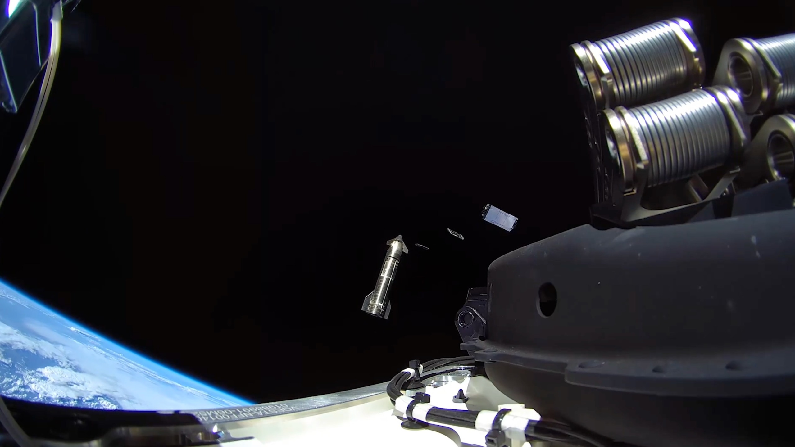 photo from a satellite in space, showing two flat satellites deploying from a large silver spacecraft with earth in the background