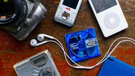 A selection of nostalgic retro late 2000s gadgets including an iPod, MiniDisc player, digital SLR, and Nintendo DS.