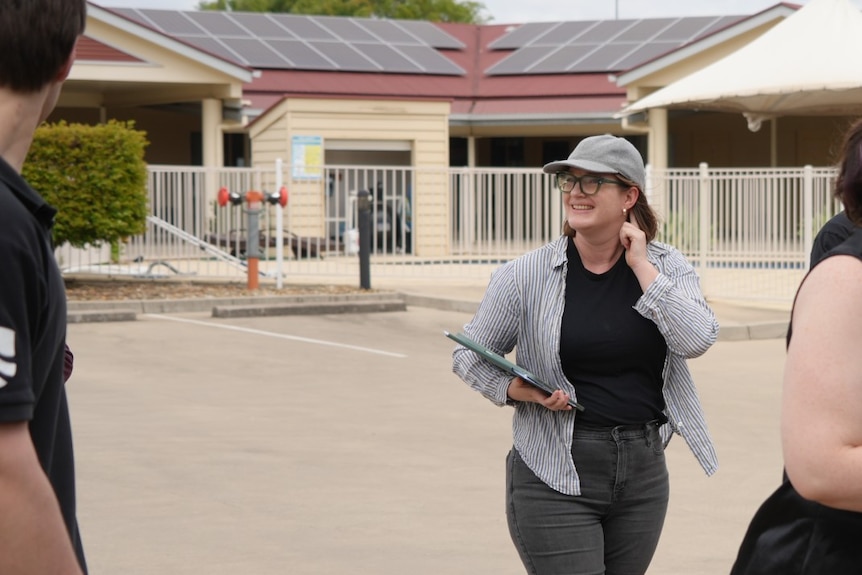 A woman stands in a car park holding a laptop.