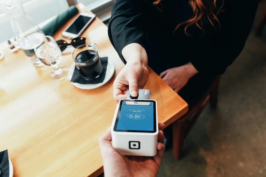 a woman with a coffee puts her credit card into an eftpos machine