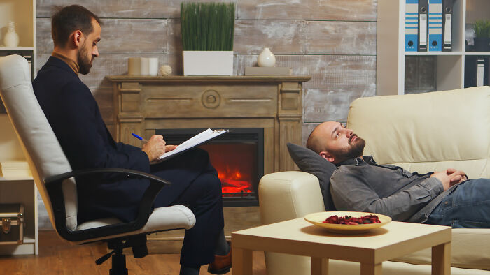 A man lying on a couch talking to his therapist in a quiet room, feeling sick and seeking help.