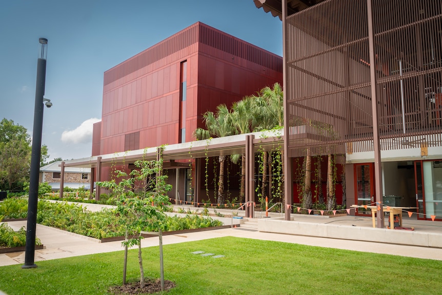 Green manicured lawns and trees foreground a modern looking building with a red exterior.