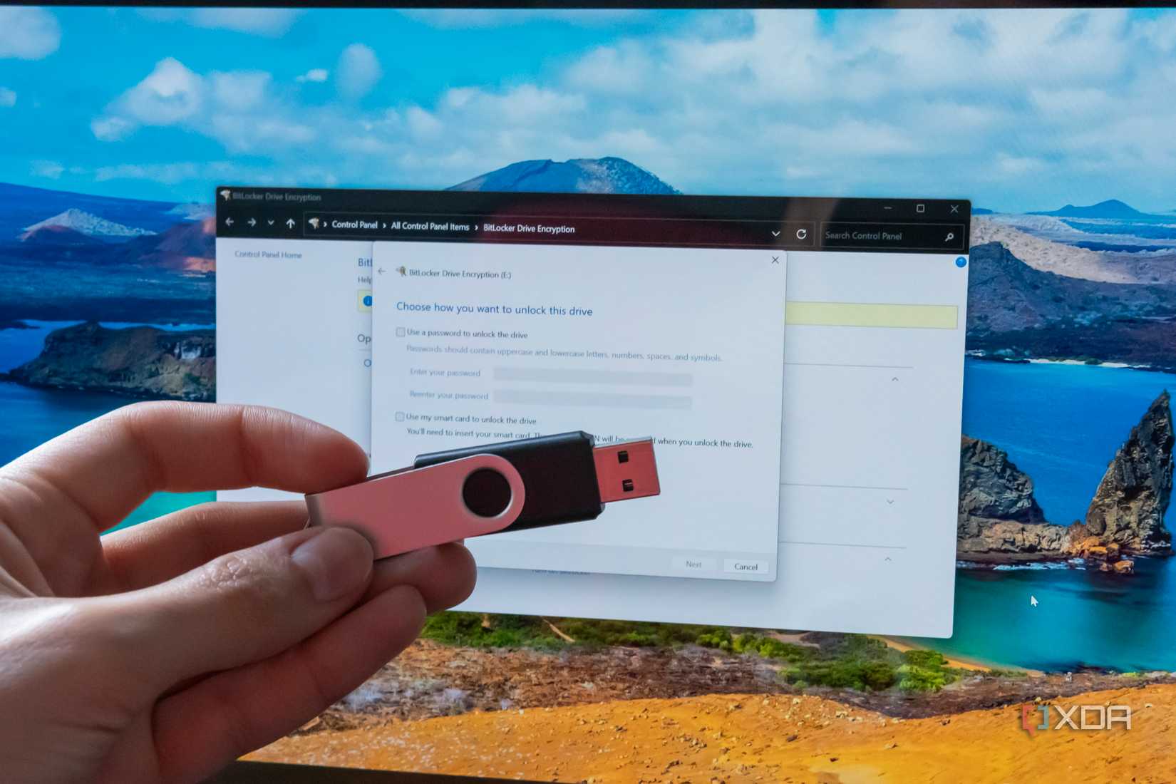 Hand holding a USB flash drive in front of a computer screen displaying BitLocker settings