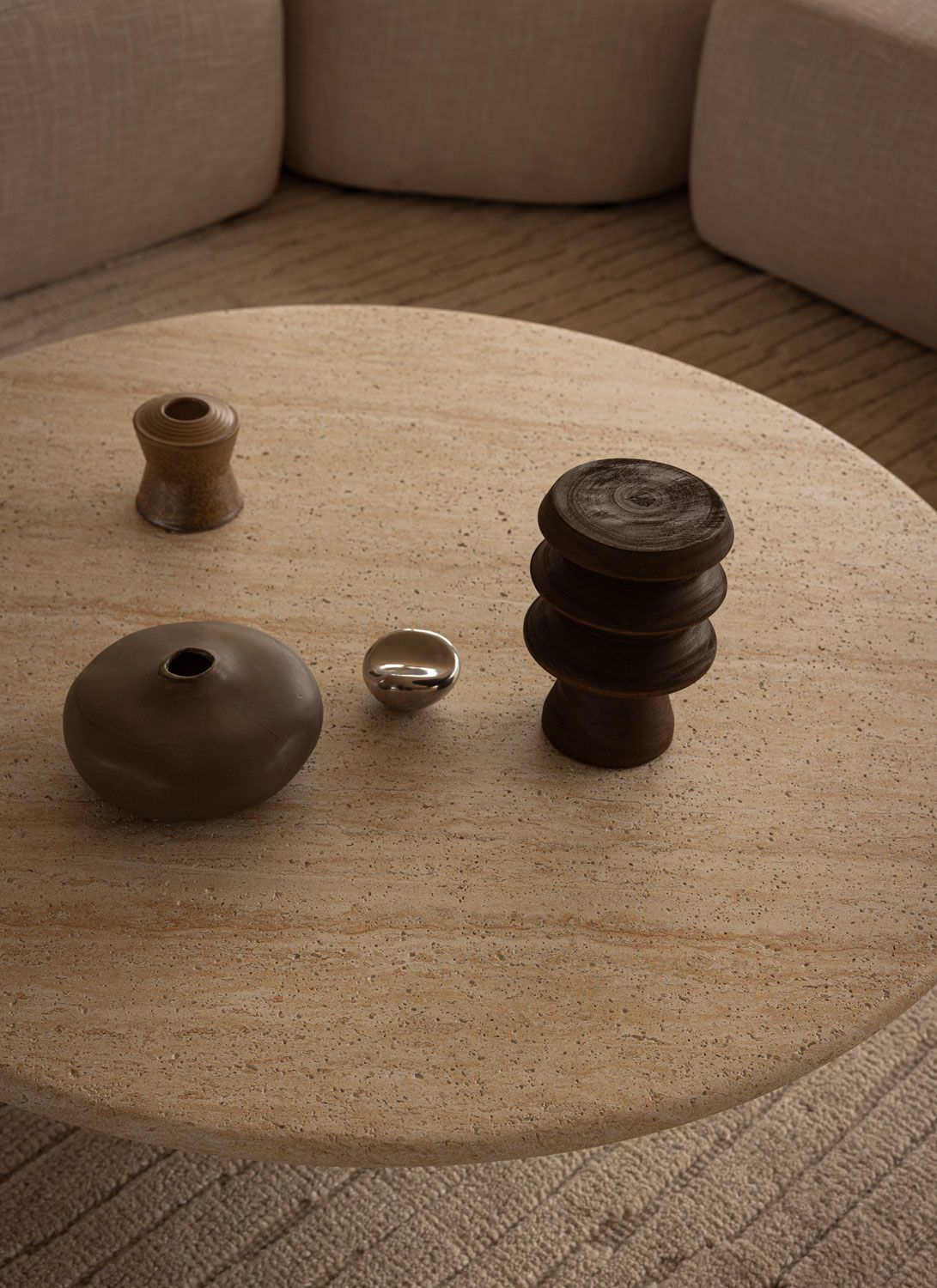 Close-up of small sculptural objects in wood, ceramic, and metal arranged on a round travertine coffee table at 262 Fifth Avenue