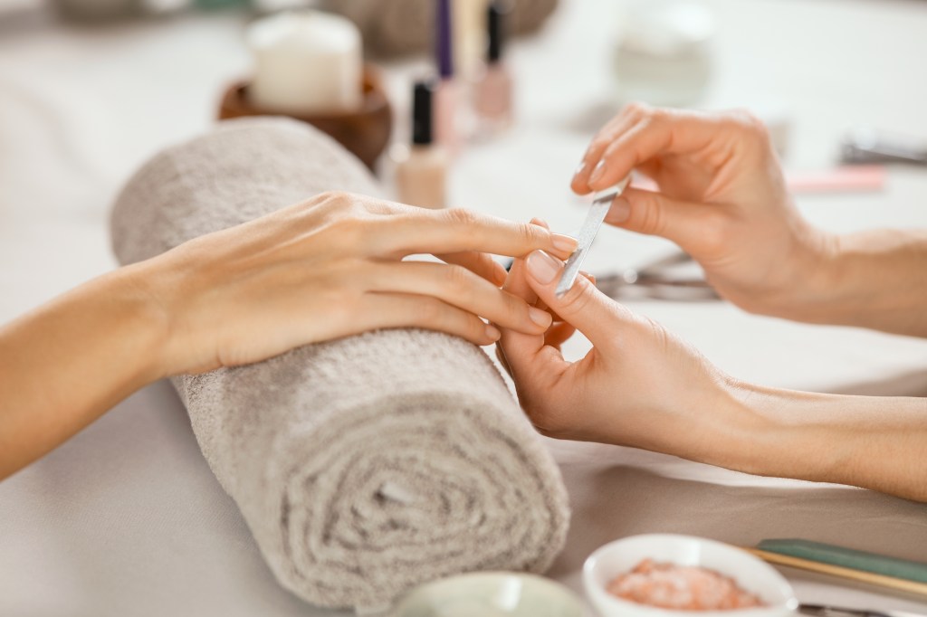A close-up of a beautician using a metal nail file on a customer's fingernails at a salon.