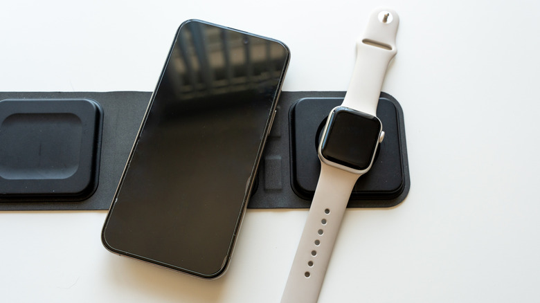 A smartwatch lying on a charging pad beside a smartphone