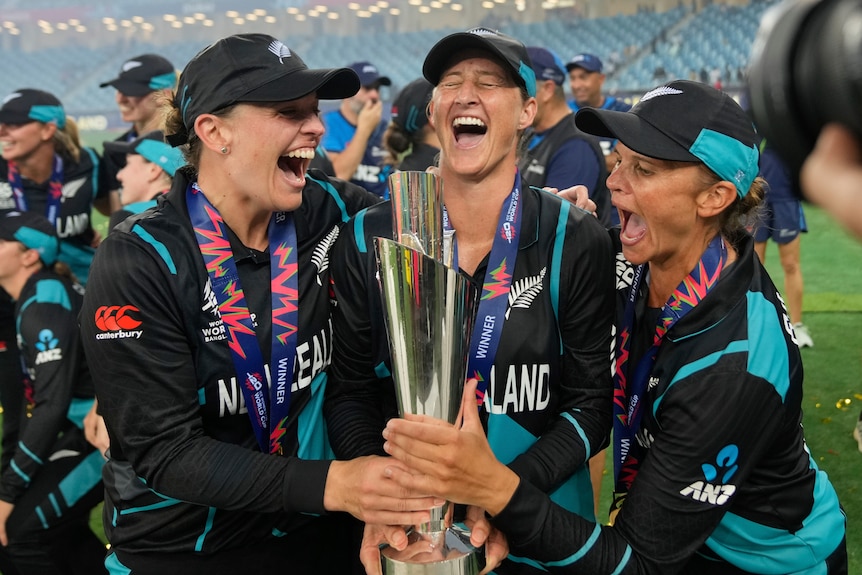 Three New Zealand cricketers smile and shout as they hold the Women's Twenty20 World Cup trophy.