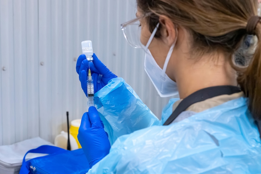 A woman wearing PPE drawing liquid into a syringe.  